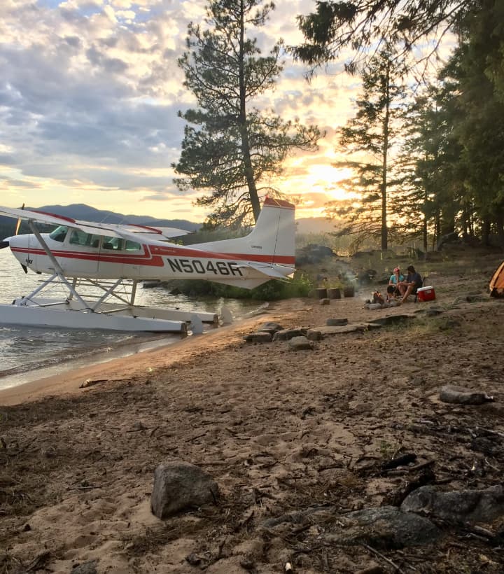 Float plane pulled up on shore and people around a camp fire.